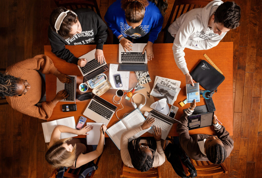 students sitting at table with books and computers